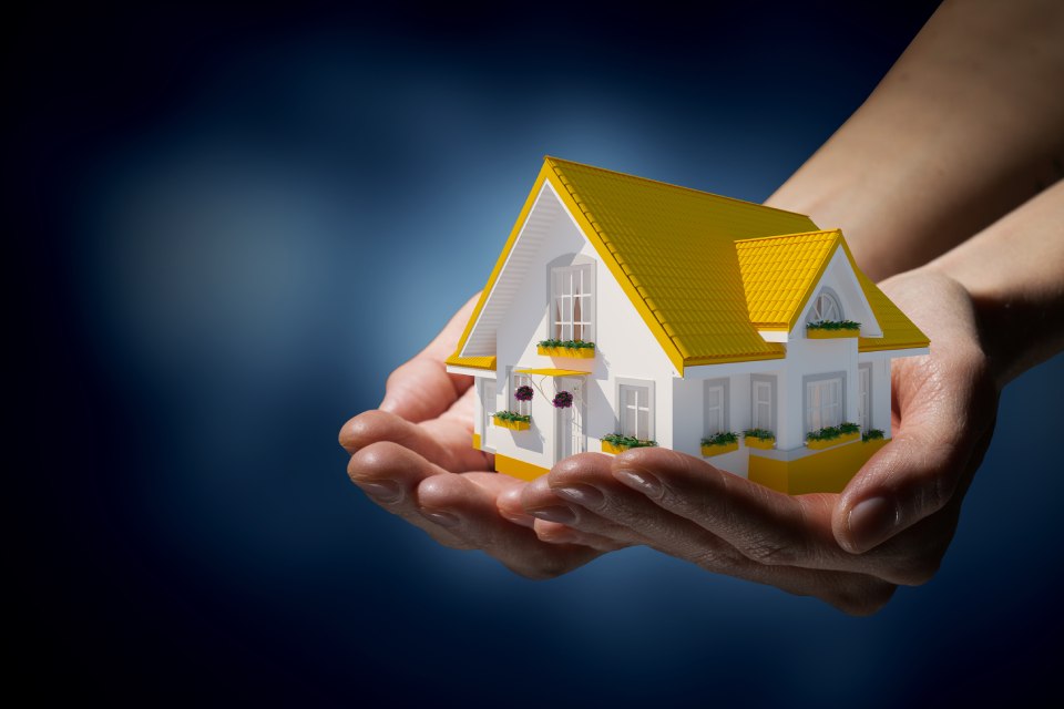 Mujer sostiene en sus manos la maqueta de una casa con tejado y cimientos de color amarillo